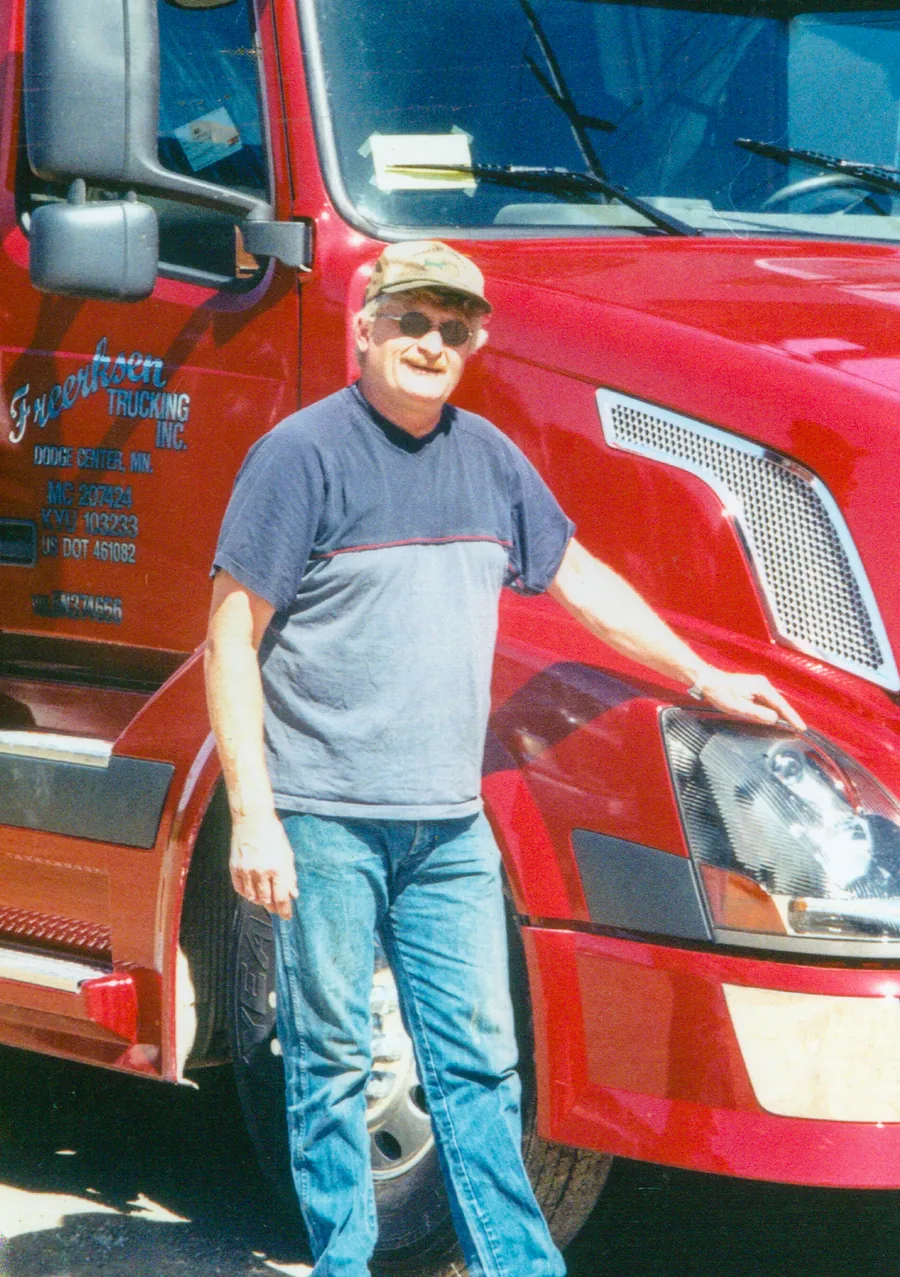 Alan Christensen smiling beside a red semi truck he drove.