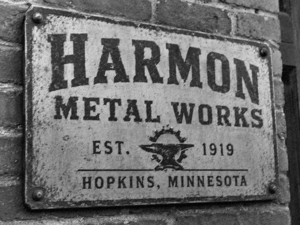 Weathered Harmon Metal Works sign mounted on a brick wall.